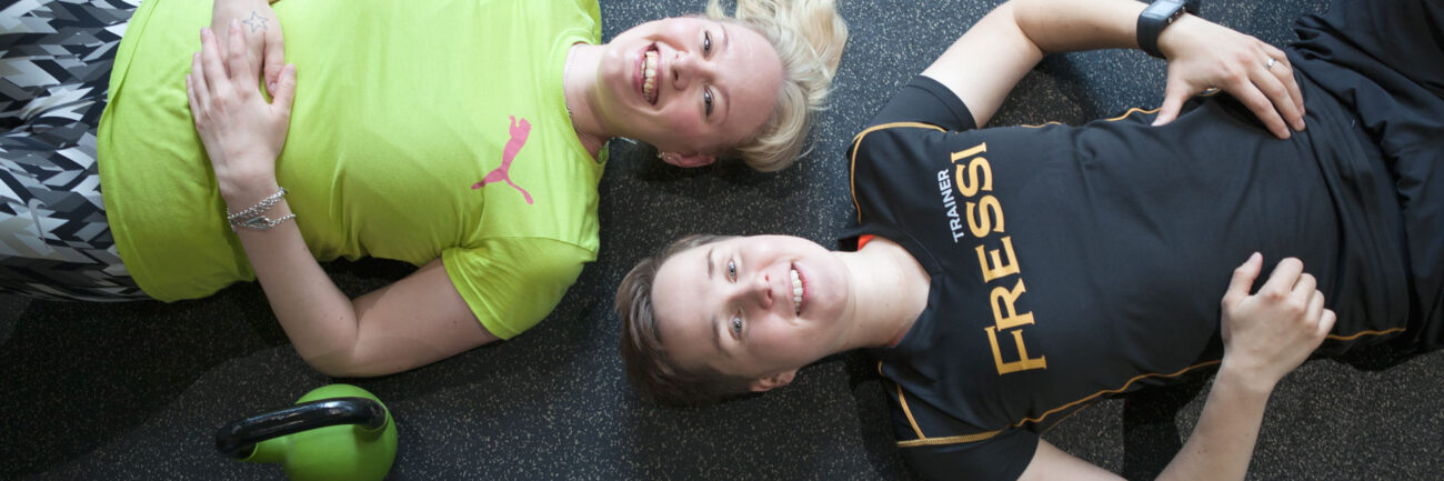 Kaksi henkilöä makaa kuntosalin lattialla.