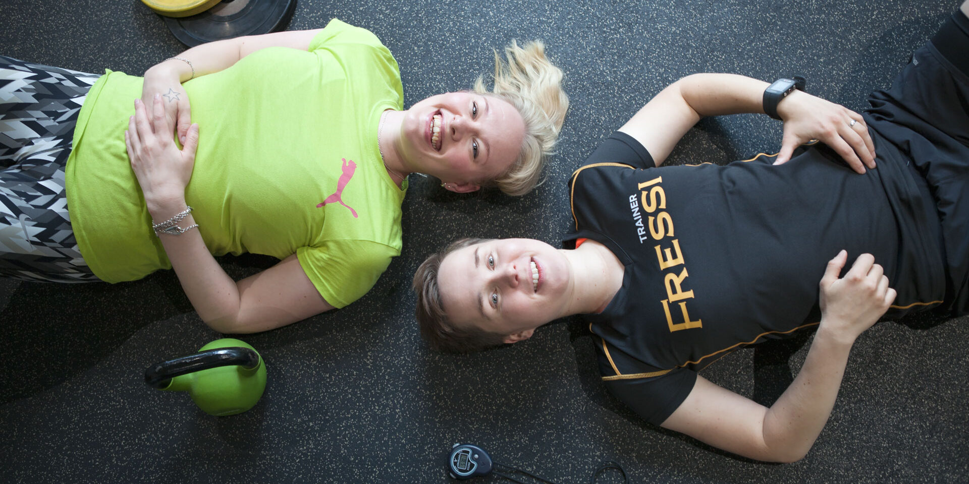 Kaksi henkilöä makaa kuntosalin lattialla.