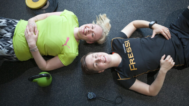 Kaksi henkilöä makaa kuntosalin lattialla.